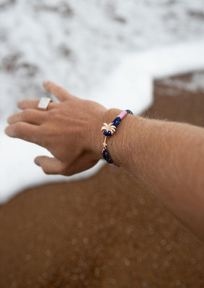 Daybreak - Single - Season two Palm anchor bracelet with pink and blue nylon band. On models hand on beach.