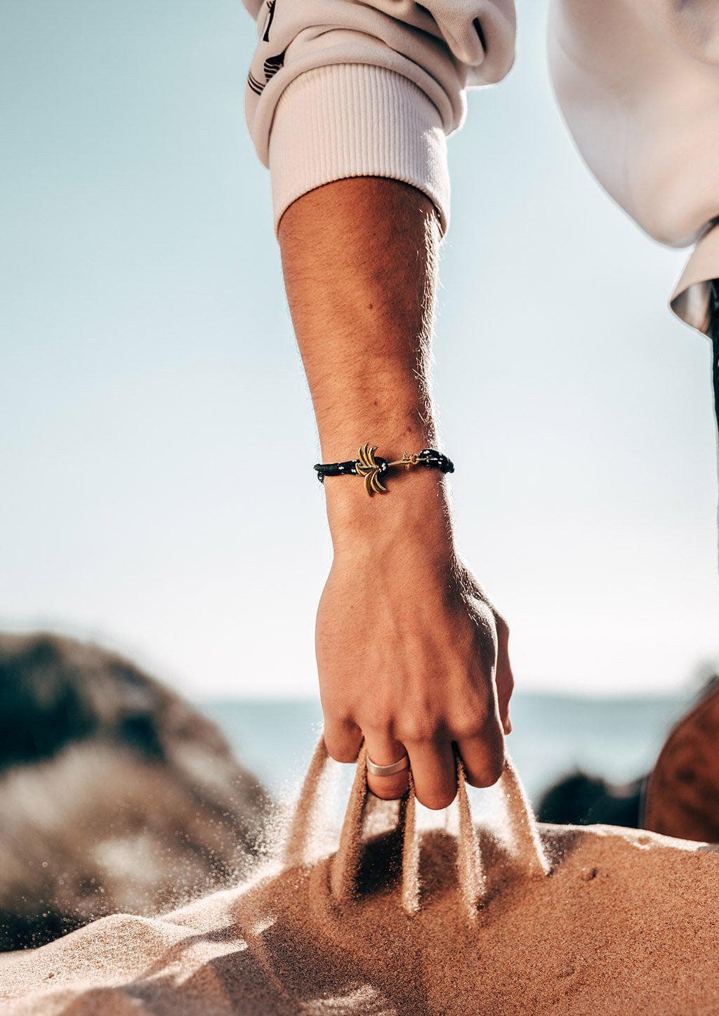 Trophy - Single - Season two Palm anchor bracelet with black and white nylon band. Male model on beach.